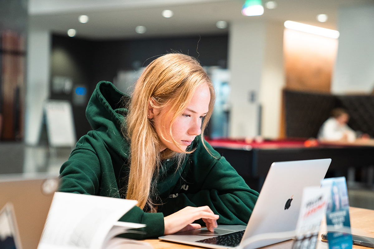 A female student wearing a green hoodie scrolls on the trackpad of a MacBook Air in Lassonde Studios. Image courtesy of the University of Utah.