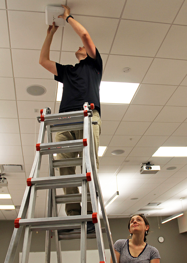 Network Core Engineer Brandon Callahan, on ladder, and student employee Gemma Grover, install APs in the Spencer Fox Eccles Business Building (SFEBB).