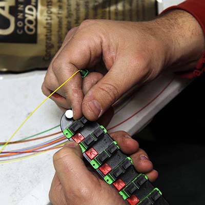 Once a feed is complete, the meticulous process of stripping, cleaning, cleaving, and fusing the fibers begins. In this file photo, optical fibers are joined to a “pigtail,” a fiber optic cable with a factory-installed connector on one end, and un-terminated fiber on the other.