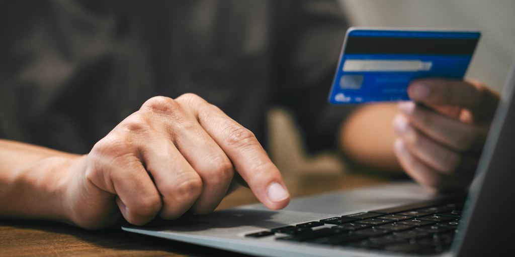 Image of a person at a computer using a credit card for an online transaction.