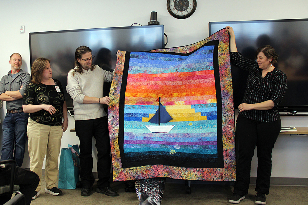 Corey Roach is presented with a handmade quilt during the outgoing chief information security officer's retirement reception on November 7.