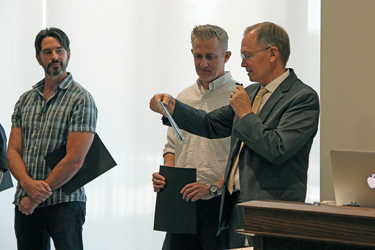 L-R: Kevin Taylor Memorial Service Award nominee Rob Birkinshaw watches as this year's award winner, Jason Moeller, listens to CIO Steve Hess read the plaque presented to Moeller at the September 17 All-Hands Meeting at the Alumni House.