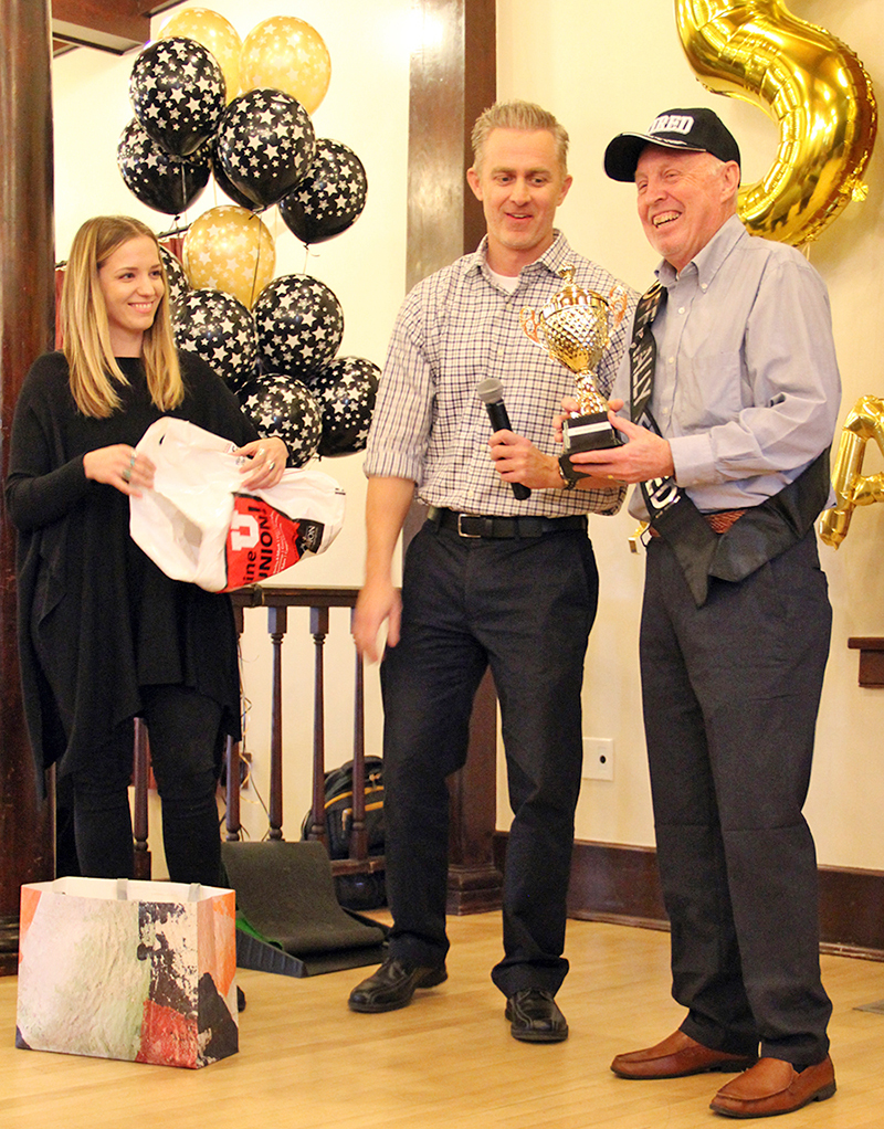 Craig Stapley, right, laughs after being presented with a trophy for "most beans counted" during his retirement party on December 20. Also pictured are Alijana Kahriman, left, and Jason Moeller, both of University Support Services.
